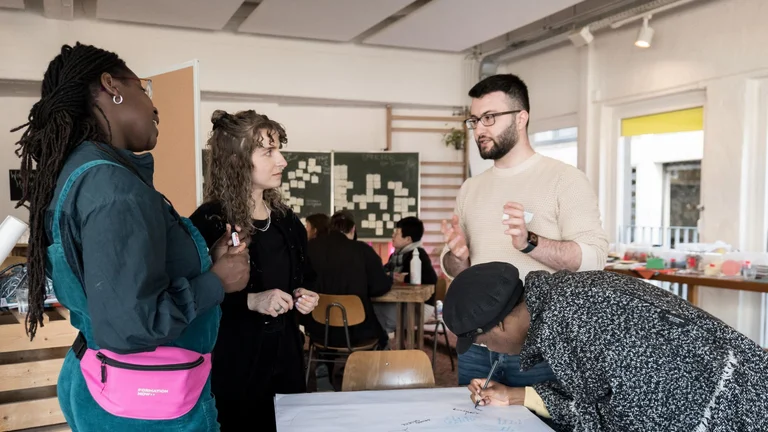 Four people think together and stand around a table with a poster on it.