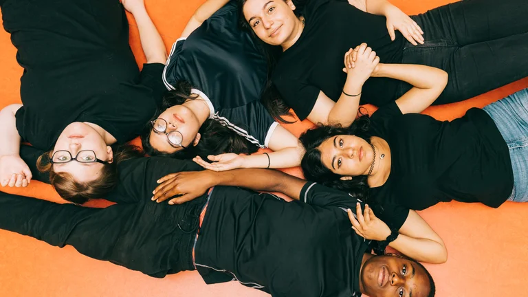 A top view of five young people lying on their backs and forming a unit.