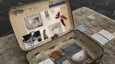 An open, old suitcase containing photographs, a diary and personal mementos.