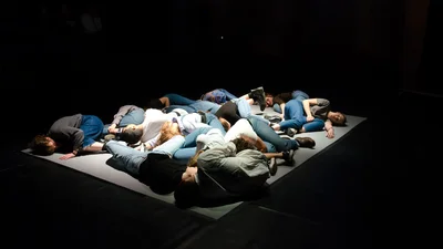 In a dark room, several people are lying on a small stage