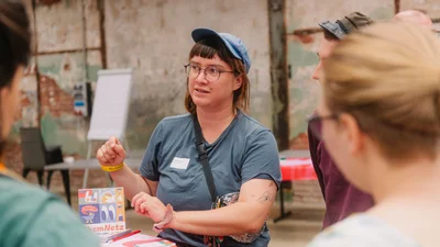 Eine Person erklärt ihr Projekt an einem Stehtisch mehreren Personen.