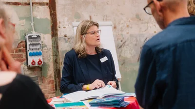eine Frau erklärt an einem Stehtisch ihre Organisation
