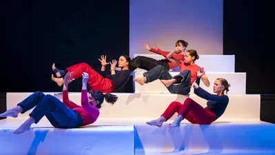 Five young women during a dance performance on a stage made up of large steps.