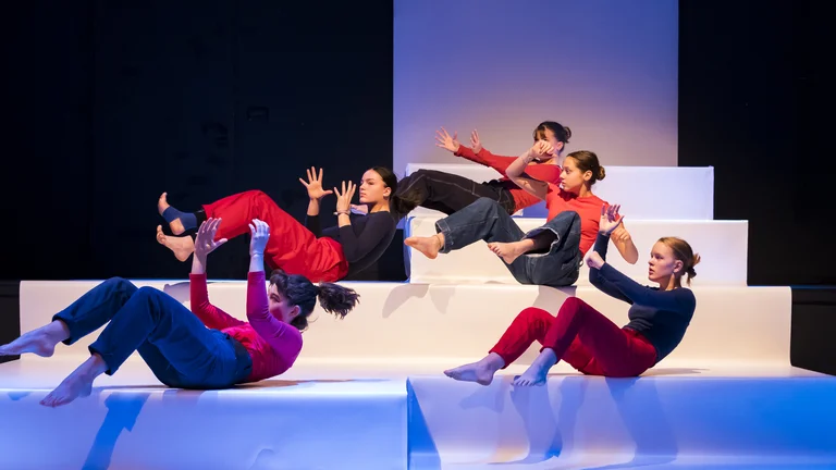 Five young women during a dance performance on a stage made up of large steps.