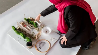 Top view of a person with a hijab pointing to a miniature model.