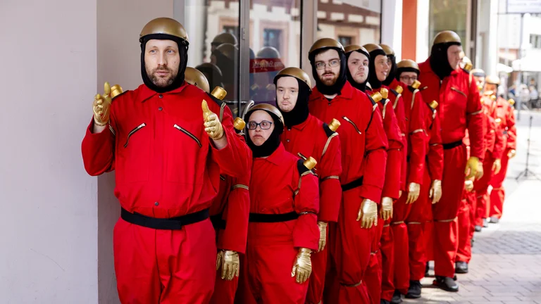 eine als Roboter verkleidete inklusive Tanzgruppe steht hintereinander aufgereiht in einer Straße