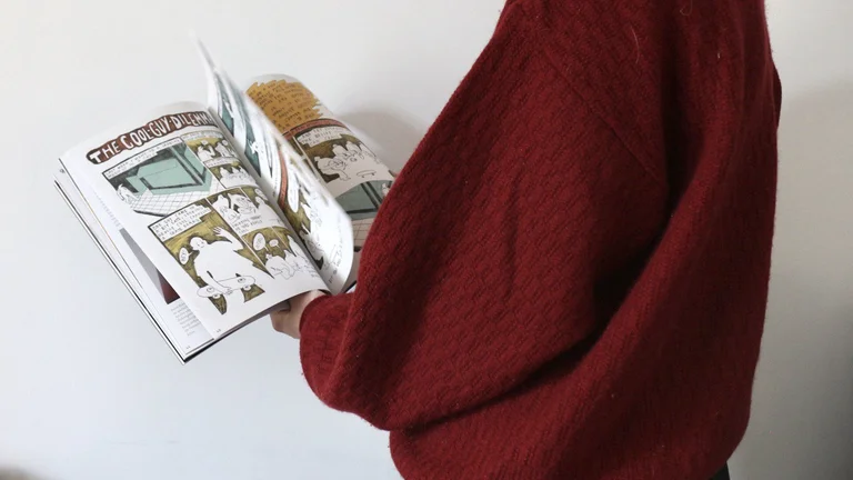 A person leafs through a magazine, two comic pages can be seen