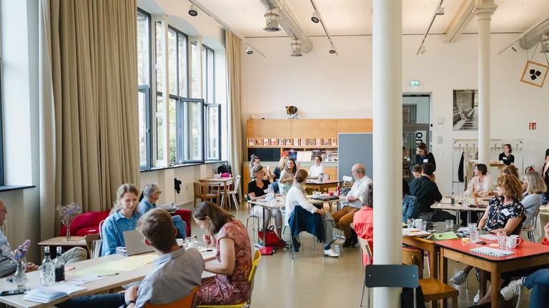 people sit at group tables in a brightly lit room
